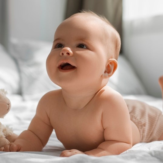 Bebê sorrindo deitado na cama com lençois brancos
